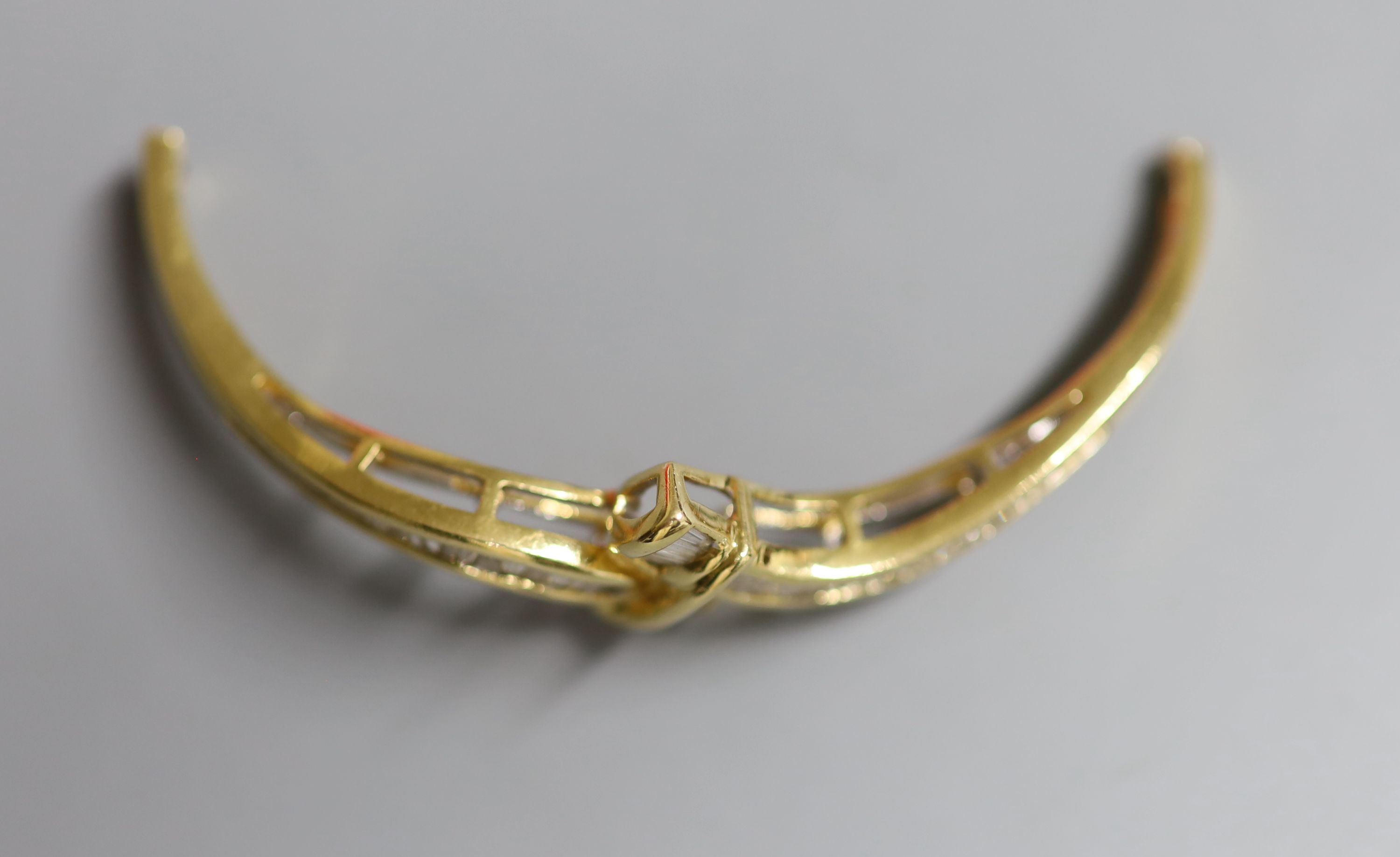 The top section only, of a yellow metal and graduated baguette cut diamond set hinged bangle, width 57mm, gross 9.1 grams.